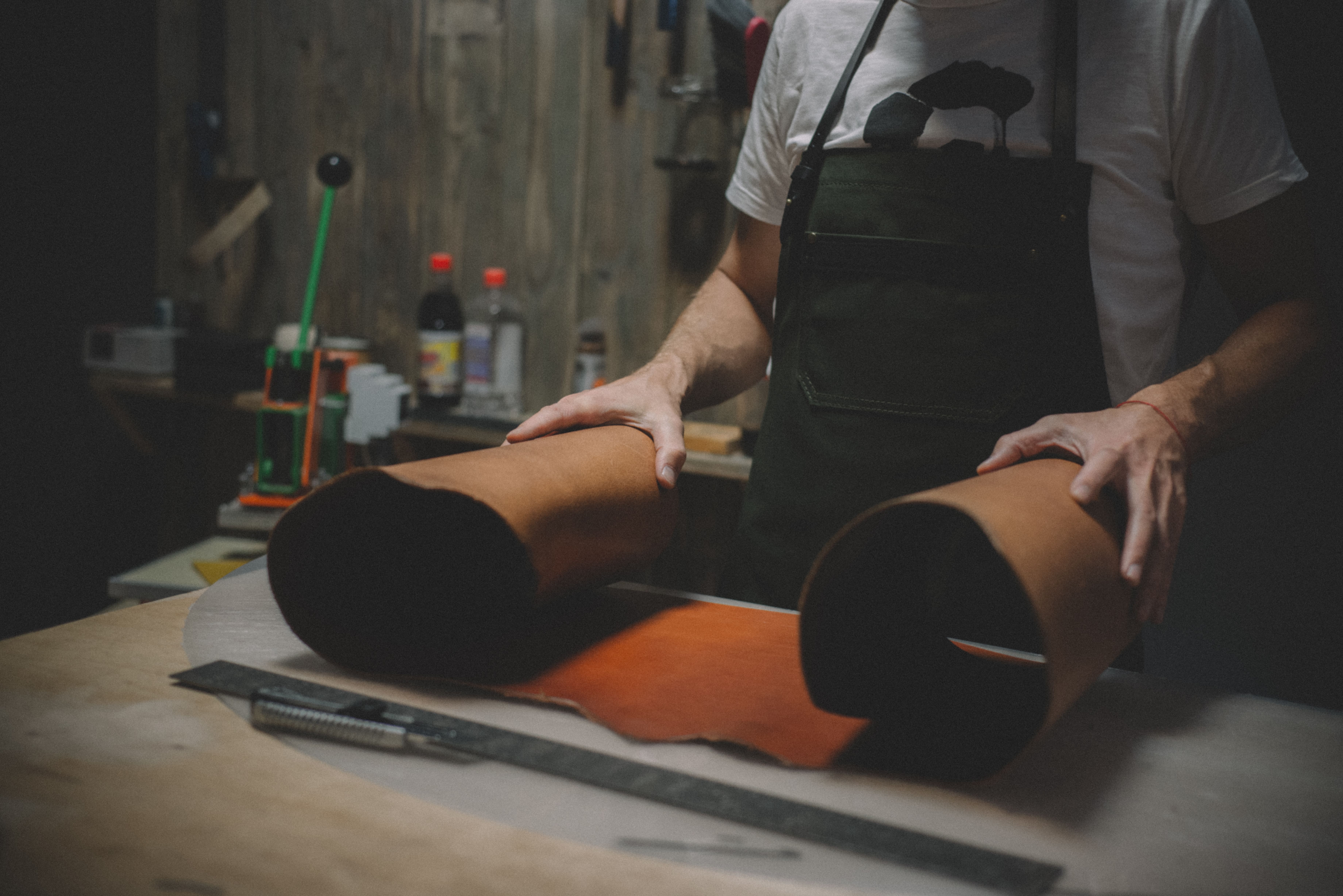 Craftsman unrolling full-grain leather hide on a workbench in a leather workshop.