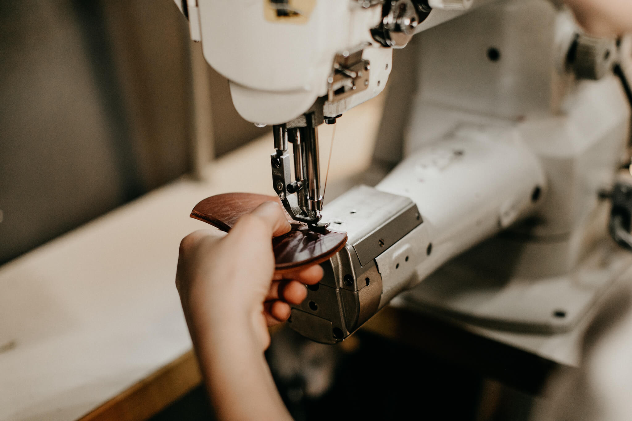 Close-up of leather being sewn with an industrial sewing machine during bag making.