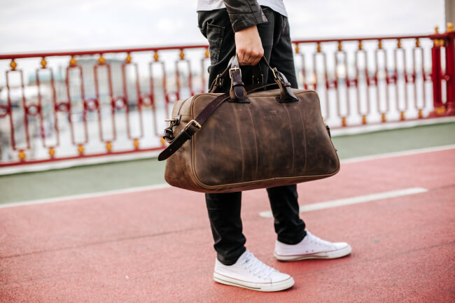 Person carrying a Kruk Garage leather Voyager Weekender Bag across a bridge, highlighting a durable and stylish travel companion.
